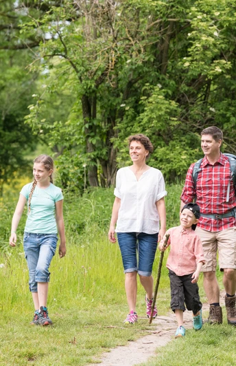 Wandern mit der Familie auf dem neanderland STEIG Familie wandert lächelnd zusammen auf einem schmalen Pfad inmitten grüner Natur im neanderland STEIG.