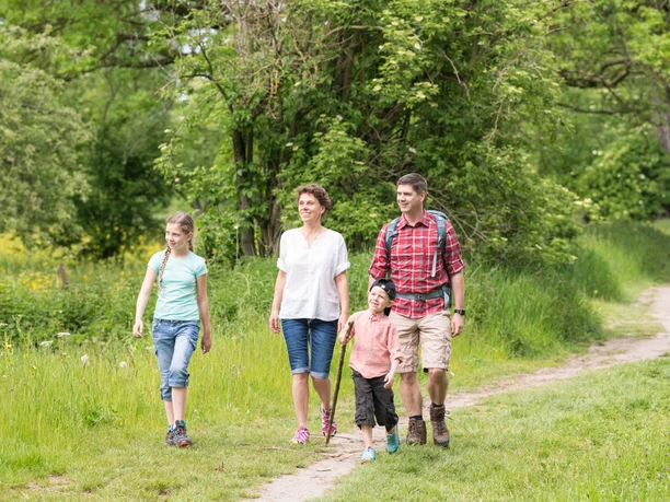 Wandern mit der Familie auf dem neanderland STEIG Familie wandert lächelnd zusammen auf einem schmalen Pfad inmitten grüner Natur im neanderland STEIG.