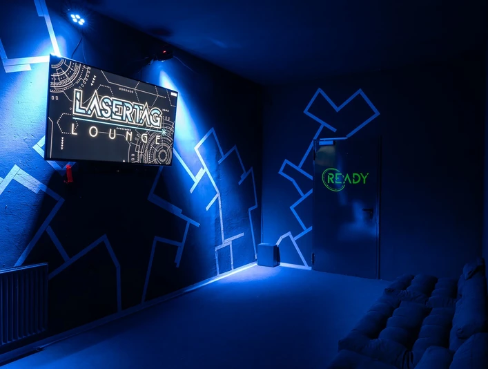 Briefingraum Ein blauer Raum mit Lasertag-Logo und Sofa an der Wand erstrahlt in Leuchtlichtern.