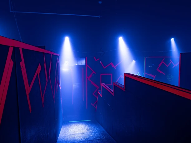 Spielflaeche Ein düster beleuchteter Raum mit roten Neonakzenten und blauen Scheinwerferlichtern.