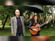 Zwei Personen im Park, eine hält eine Gitarre, die andere einen Regenschirm über beide.