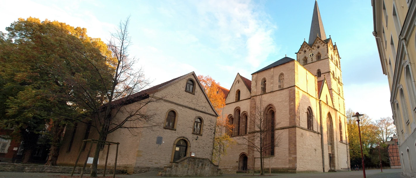 Historische Kirche mit gotischem Turm, umgeben von Herbstbäumen und Kopfsteinpflasterweg.