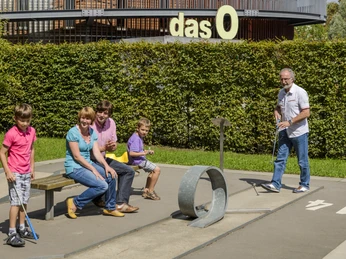 Minigolf im O-Schatz-Park - Freizeit in der Leipzig Region Familie spielt Minigolf, Im Hintergrund die Multifunktionshalle "das O", Freizeit, Tierpark, Familienausflug