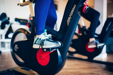 Fitness Gezeitenland (2).jpg Auf dem Bild sind die Beine einer Person auf einem Fitness-Fahrrad zu sehen, fokussiert auf die Pedale.