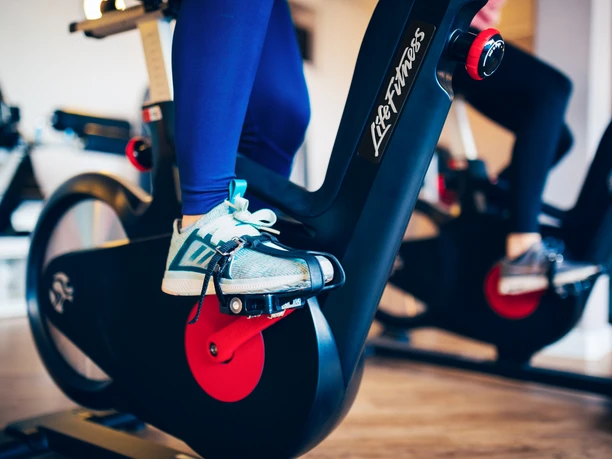 Fitness Gezeitenland (2).jpg Auf dem Bild sind die Beine einer Person auf einem Fitness-Fahrrad zu sehen, fokussiert auf die Pedale.