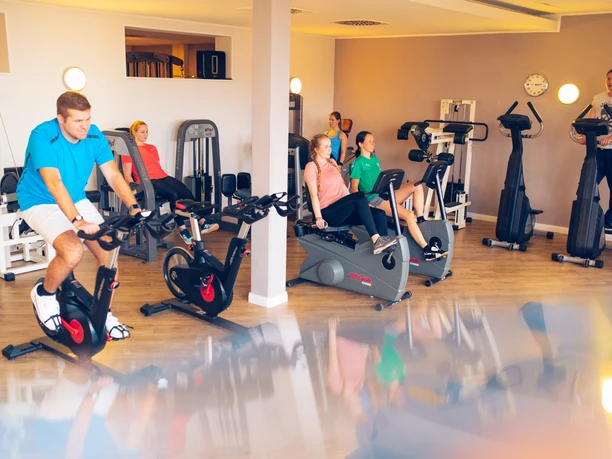 Fitness room at Gezeitenland Borkum with modern training equipment and athletes doing fitness activities.