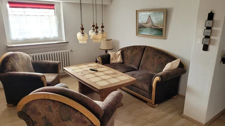 1000112968.jpg Wohnzimmer mit zwei Sesseln, einem Sofa und einem Couchtisch, dekoriert mit hängenden Lampen.