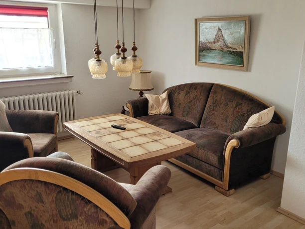 1000112968.jpg Wohnzimmer mit zwei Sesseln, einem Sofa und einem Couchtisch, dekoriert mit hängenden Lampen.