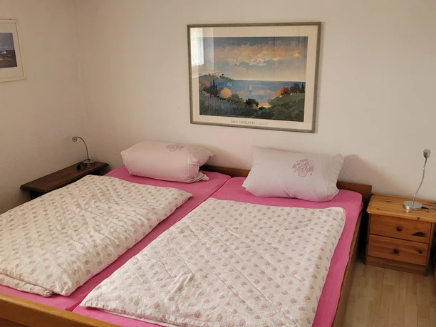 1000112970.jpg Ein Schlafzimmer mit rosafarbenem Doppelbett, Leselampen und Landschaftsgemälden an den Wänden.