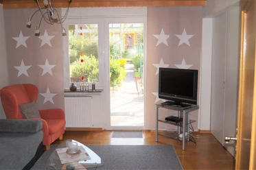 IMG-20250321-WA0010.jpg Ein Wohnzimmer mit einem grauen Sofa, einem roten Sessel und einem Fernseher vor einem großen Fenster.