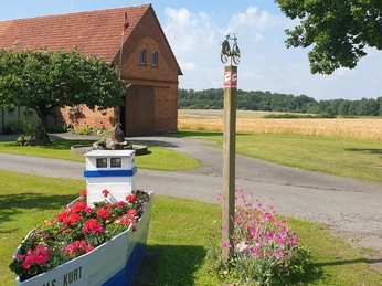Ein rot-brick Lagerhaus, blühender Pflanzkasten im Boot, Weg und grüne Wiese im ländlichen Bereich.