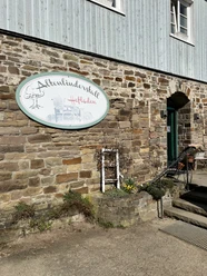 Hofladen Altenlinderstall Hofladen Altenlinderstal im rustikalen Steingebäude mit beschildertem Eingang und blühenden Blumen.