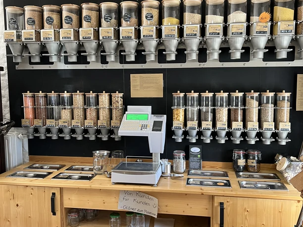 Hofladen Altenlinderstall Ein Unverpackt-Laden mit Holzregalen, gefüllt mit Spendern für Bio-Lebensmittel in verschiedenen Sorten.