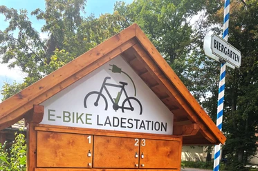 E-Bike Ladestationen bei den Sieben Holzhütte mit E-Bike-Ladestation, umgeben von Bäumen; nahe einem Biergarten gelegen.