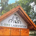 E-Bike Ladestationen bei den Sieben Holzhütte mit E-Bike-Ladestation, umgeben von Bäumen; nahe einem Biergarten gelegen.