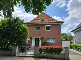 Ein modernes, rotes Ziegelhaus mit einem Satteldach. Umgeben von Bäumen und bunten Blumen im Garten.