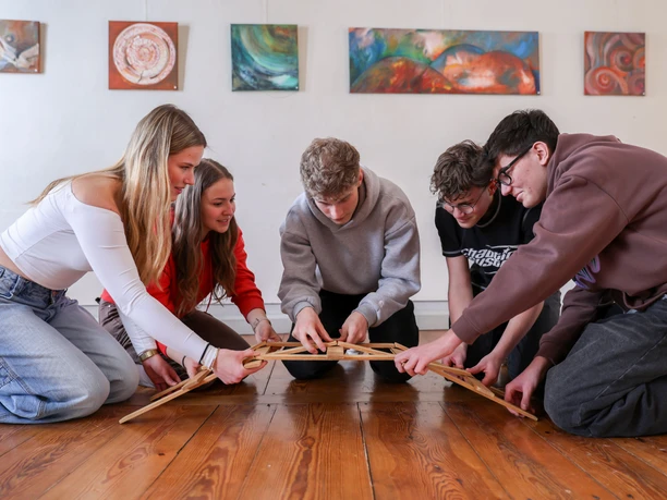Na obrázku je pět mladých lidí, kteří společně zvládli úkol v rámci workshopu na zážitkové výstavě Kořeny a křídla.