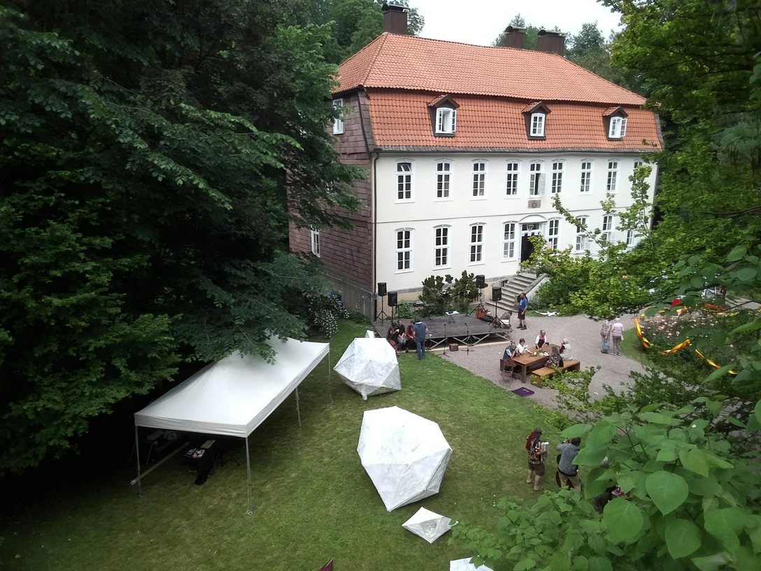 Wasserschloss Reelkirchen © Wasserschloss Reelkirchen.jpg Menschen genießen ein Fest im Garten eines historischen Gebäudes mit rotem Dach und weißen Wänden.