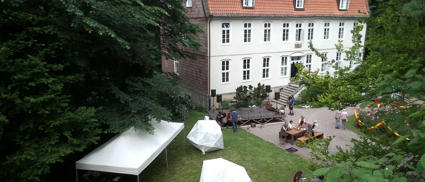 Wasserschloss Reelkirchen © Wasserschloss Reelkirchen.jpg Menschen genießen ein Fest im Garten eines historischen Gebäudes mit rotem Dach und weißen Wänden.