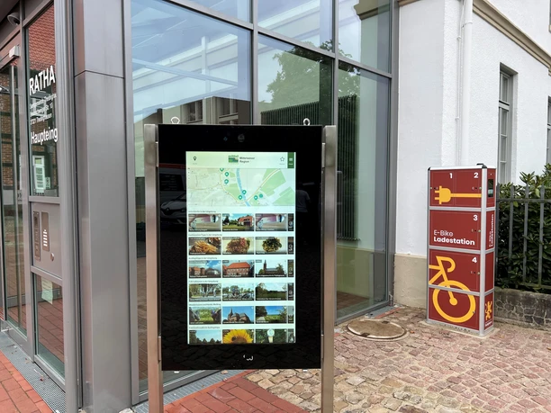 Information kiosk in front of City Hall in Thedinghausen, featuring a digital map and an e-bike charging station on the right.