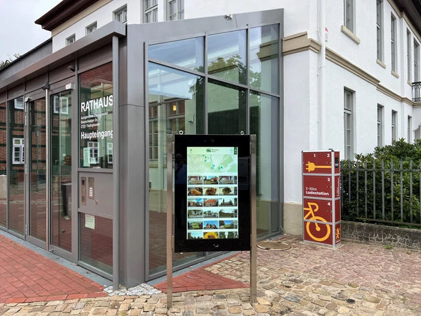 Information kiosk in front of Thedinghausen City Hall with a digital display and an adjacent bike charging station.