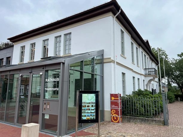 Information kiosk at the historic town hall in Thedinghausen, set against a modern glass addition; trees on the left, on the right.