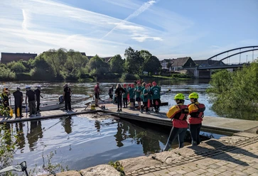 2. Beverunger Drachenbootregatta auf der Weser Menschen bereiten sich auf einer Plattform am Flussufer mit Drachenbooten auf ein Rennen vor.
