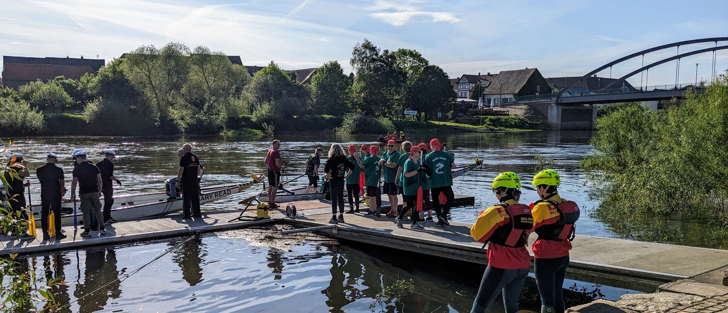 2. Beverunger Drachenbootregatta auf der Weser Menschen bereiten sich auf einer Plattform am Flussufer mit Drachenbooten auf ein Rennen vor.