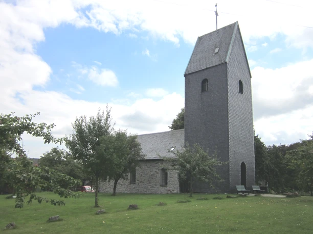 Windrather Kapelle, Velbert Historische Kapelle in Velbert mit steinverkleidetem Turm umgeben von grüner Wiese und Bäumen.