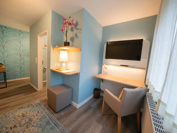 Hotel Beckord, Altdeutscher Hof Helles Hotelzimmer mit Schreibtisch, Wand-TV, Sessel, Regal und Badzugang