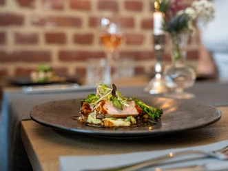 Restaurant Ohters Ein elegant angerichtetes Gericht mit zartem Fleisch, Gemüse und Beilage auf einem schwarzen Teller.