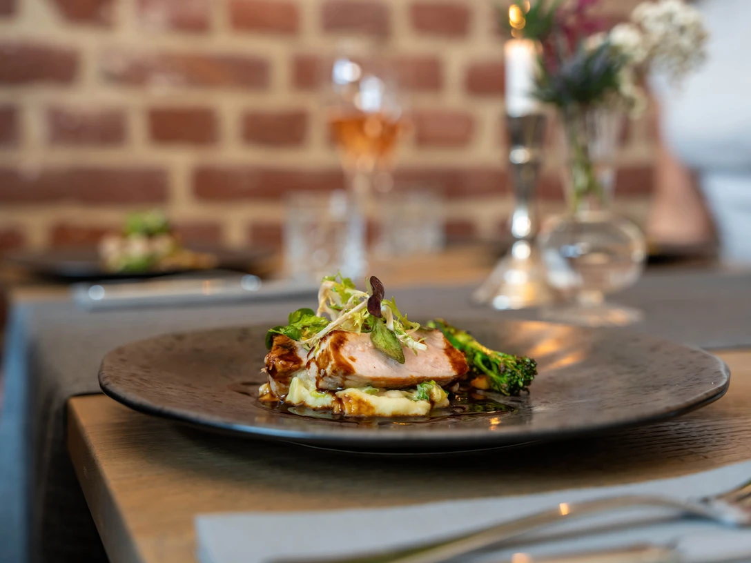 Restaurant Ohters Ein elegant angerichtetes Gericht mit zartem Fleisch, Gemüse und Beilage auf einem schwarzen Teller.