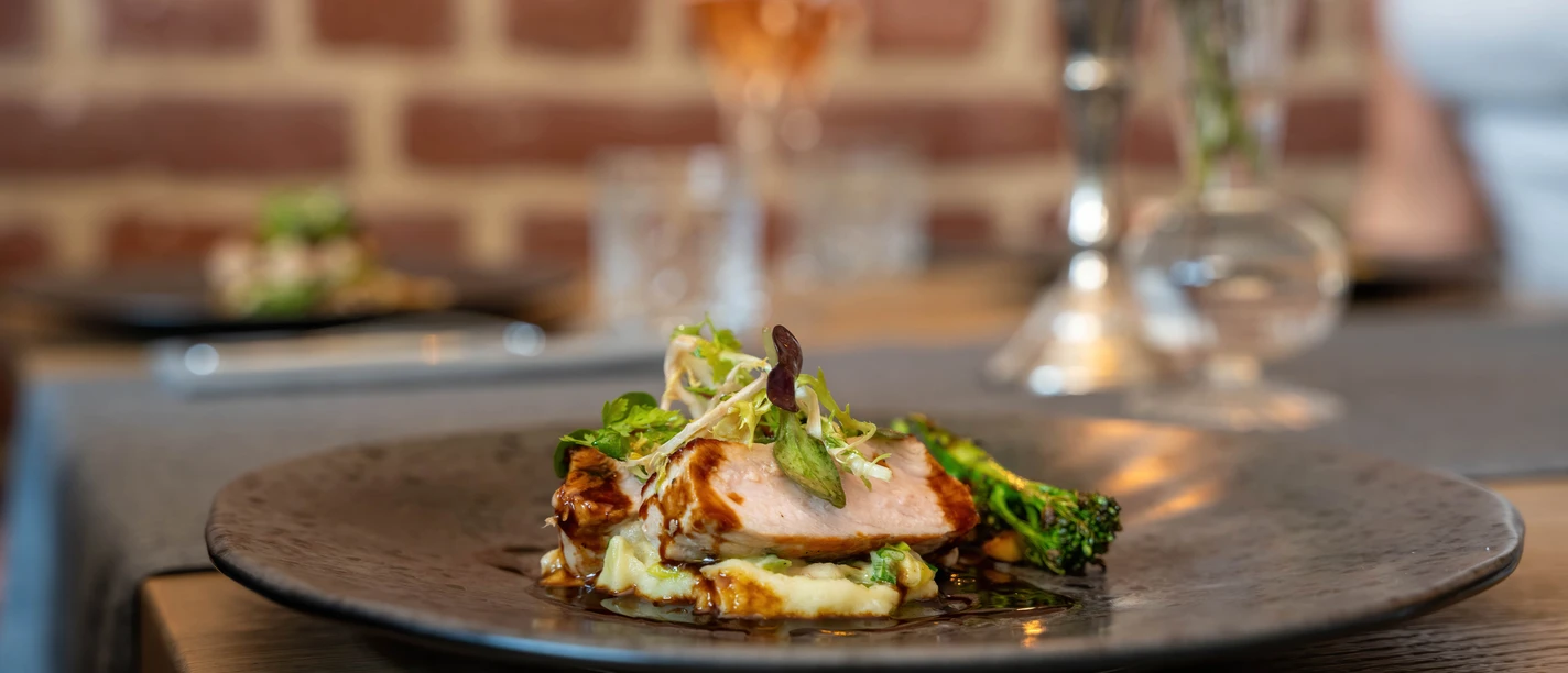 Restaurant Ohters Ein elegant angerichtetes Gericht mit zartem Fleisch, Gemüse und Beilage auf einem schwarzen Teller.
