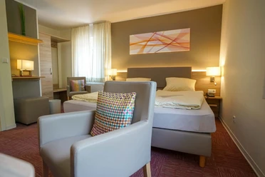 Modernes Hotelzimmer mit Doppelbett, Sitzbereich, Schreibtisch, Fenster und dezenter Wandkunst.