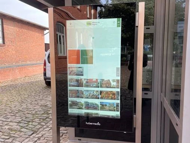 Infoterminal Bruchhausen-Vilsen Infoterminal mit Bildschirm vor einem Backsteingebäude, zeigt digitale Informationen und Fotos.