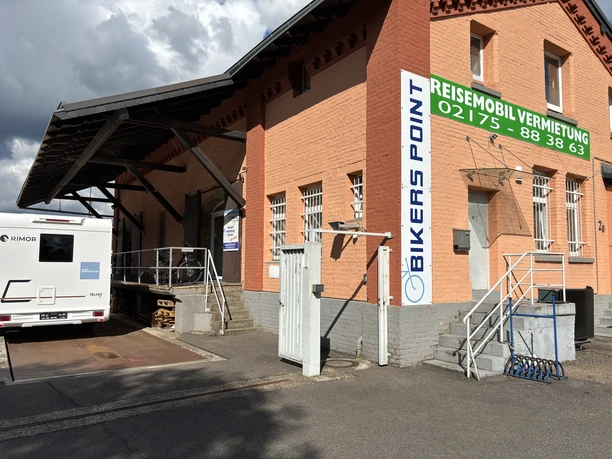 Bikers Point Ein rotes Backsteingebäude mit der Aufschrift "Bikers Point" und einer Einfahrt für Wohnmobile.