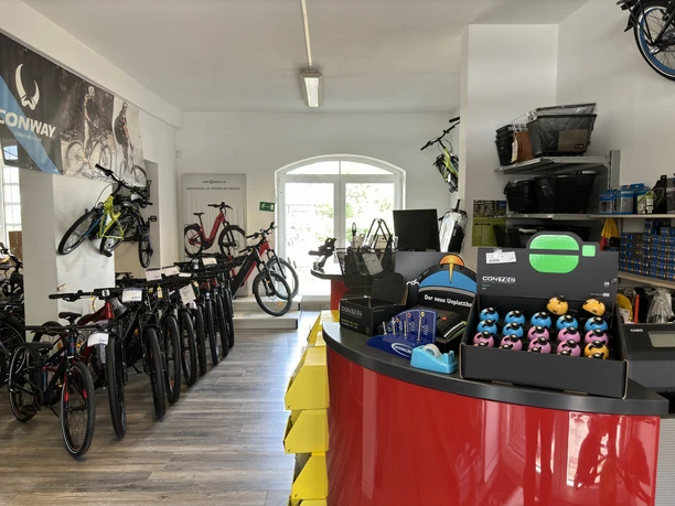 Bikers Point Fahrradladen mit verschiedenen Fahrrädern und Zubehör auf hölzernem Boden, freundlich beleuchtet.