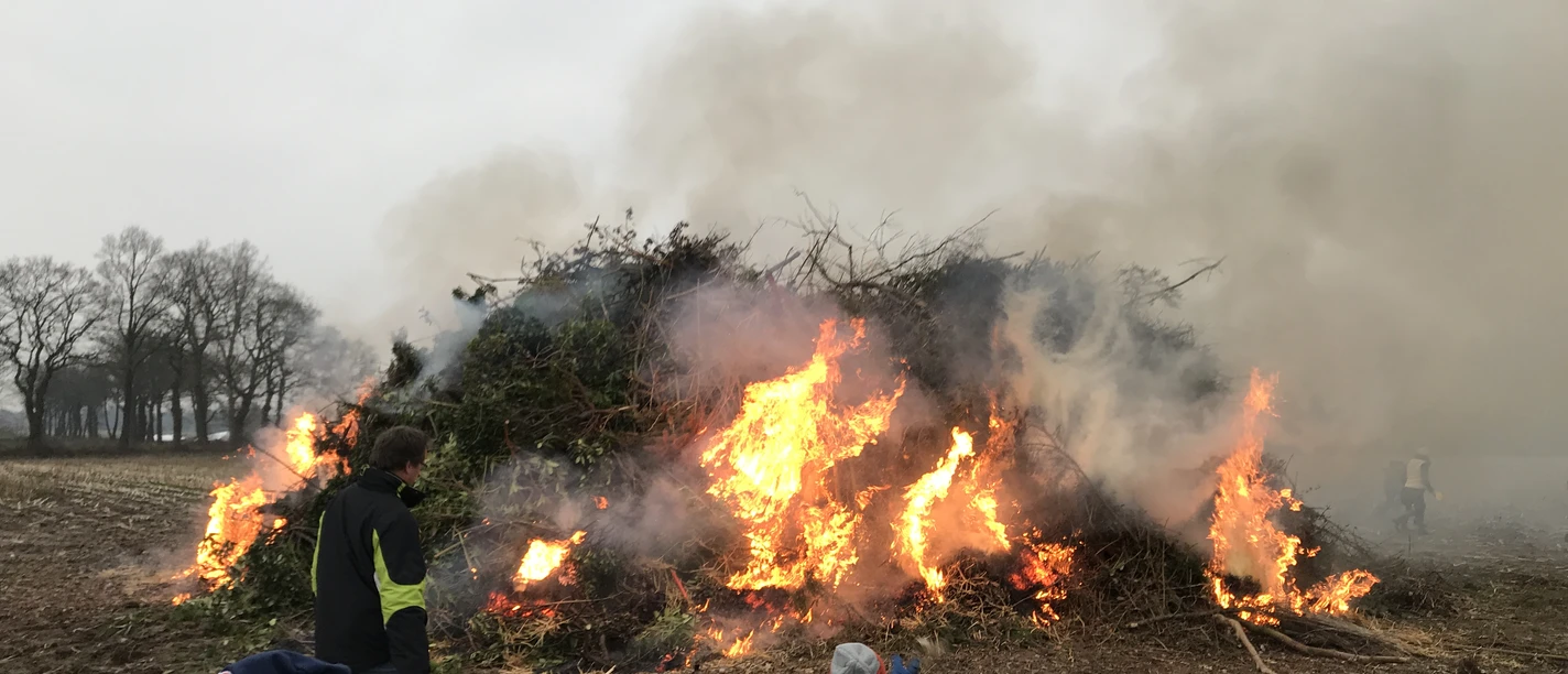 Osterfeuer Backemoor Großes, rauchendes Osterfeuer auf einem Feld. Im Vordergrund betrachten Menschen die Flammen.