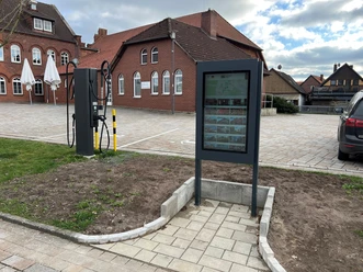 An information kiosk in front of red brick buildings, with cobblestone streets and bicycle accessories in a square.