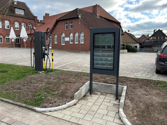Infoterminal Rehburg Infoterminal vor roten Backsteingebäuden mit Kopfsteinpflaster und Fahrradzubehör auf einem Platz.