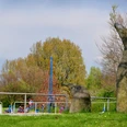 Ein Abenteuerspielplatz mit Klettergerüst, Felsen im Vordergrund und spielenden Kindern im Hintergrund.