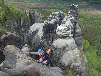 geführte Stiegentour Tourengeher erklimmen über Leitern steile Felsen in der Sächsischen Schweiz, umgeben von grünen Wäldern.