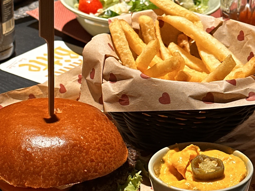 Burgerheart in Monheim Mitte Ein Burger mit Salat, einer Portion Pommes frites und Käsesauce in einem Restaurant.