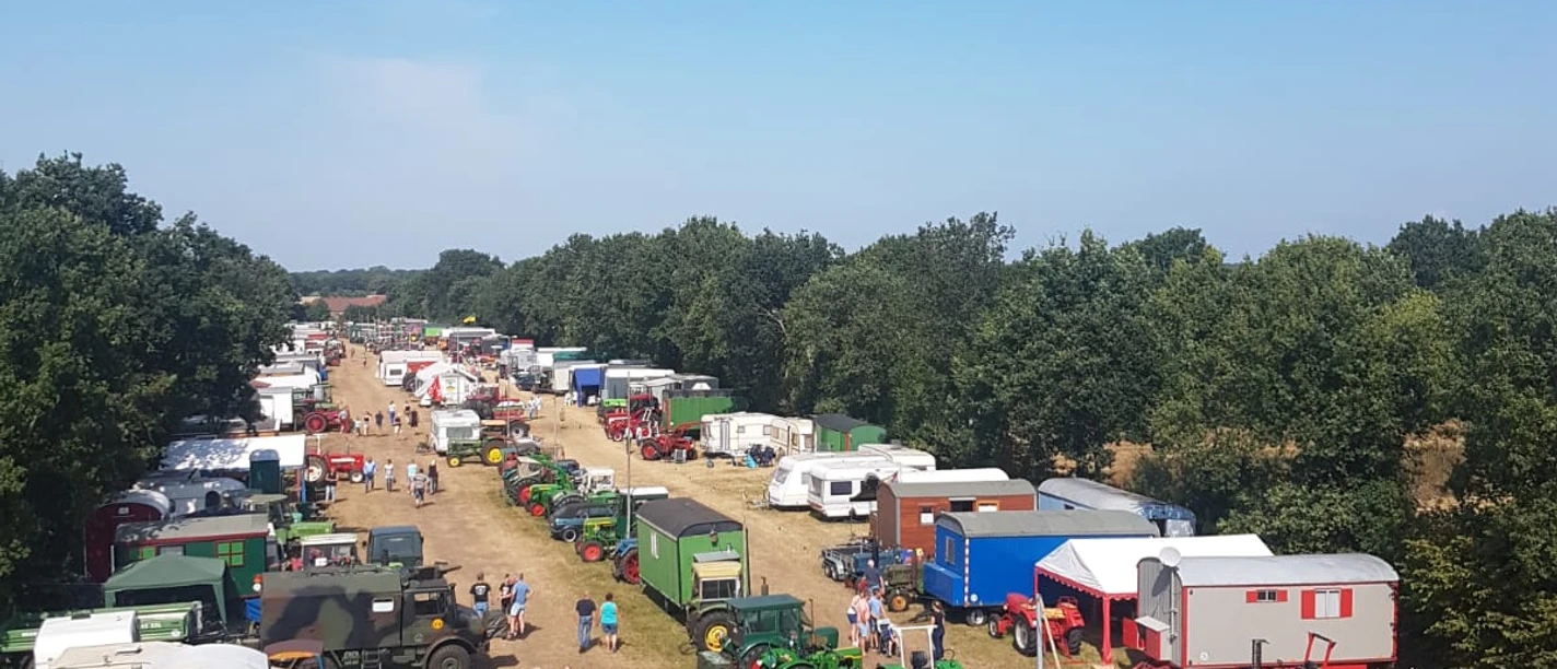 Zwischenberger Fest 2.jpg Eine ländliche Szene mit einer langen Reihe von Traktoren und Anhängern auf einem Feld, umgeben von Bäumen.