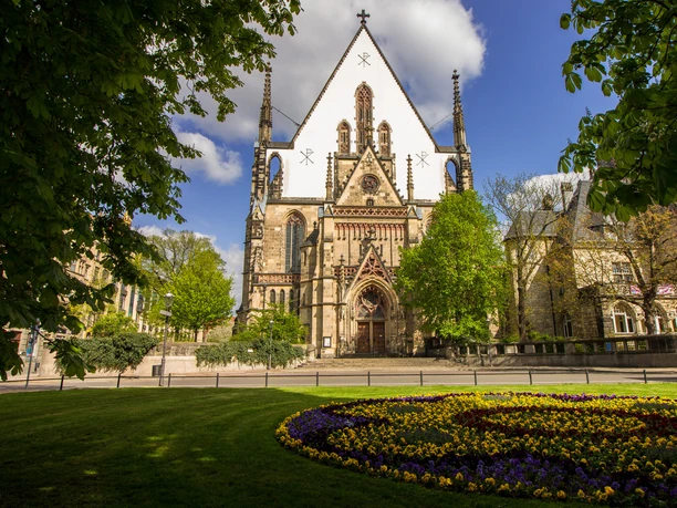 Thomaskirche Leipzig - City of Music Leipzig View of the Thomaskirche Leipzig framed by green trees, in front of it a meadow planted with pansies, City of Music Leipzig, Sightseeing