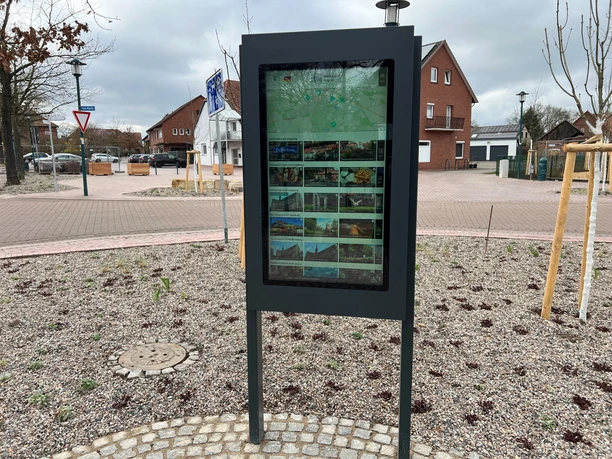 An information kiosk displaying digital information, surrounded by paved paths in a suburb.