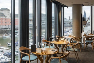ox&klee Blick in ein stilvolles Restaurant mit großen Fensterfronten. Im Hintergrund Hafen und Domspitzen.