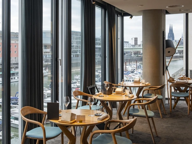 ox&klee View into a stylish restaurant with large window fronts. Harbor and cathedral spires in the background.