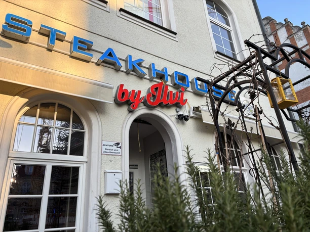 Der Eingang des Steakhouse by Ilvi in Herford mit auffälliger Beschilderung und großen Fenstern.