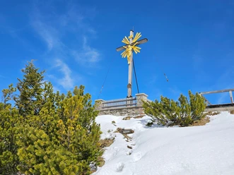 Gipfelkreuz Wank Holzernes Gipfelkreuz mit goldener Figur über verschneiter Bergflanke unter klarem Himmel